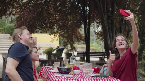 young caucasian boy taking selfie with his family during an outdoor dinner