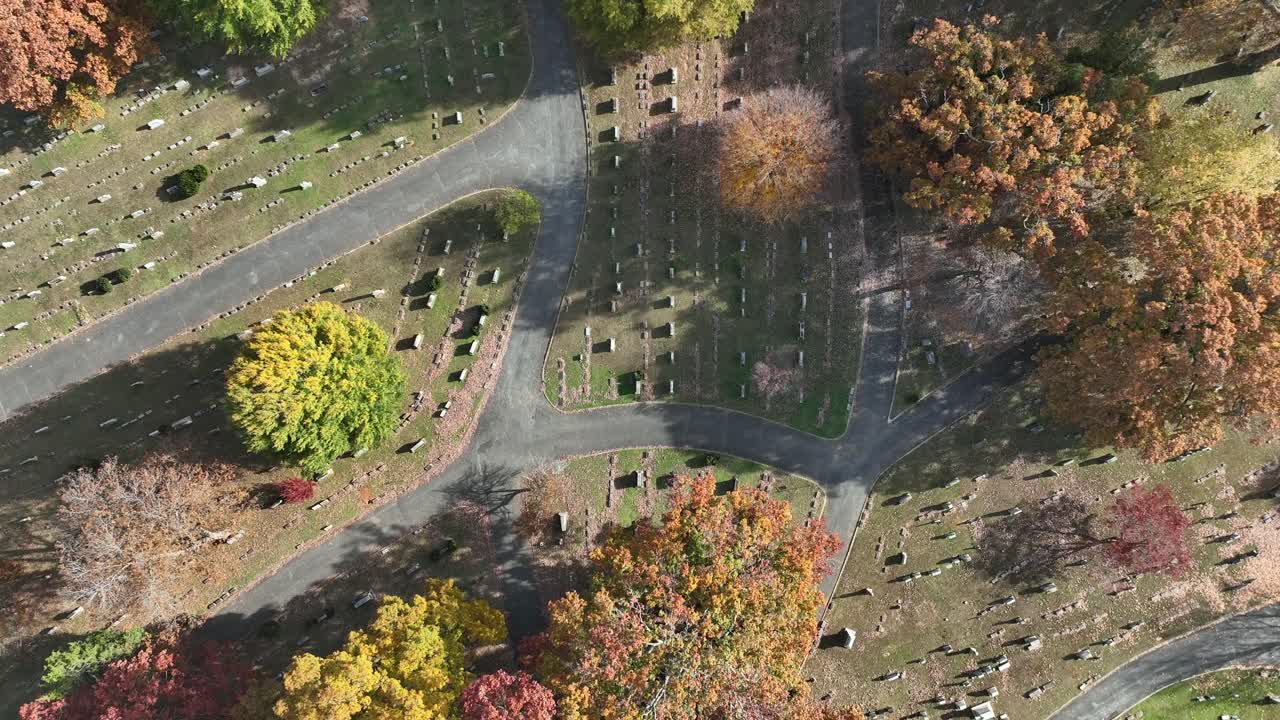 Autumn cemetery in United States seen above, with intersecting paths, gravestones and colorful fall trees Calm aerial drone top down on sunny day in fall. Rising shot
