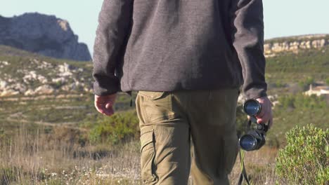 hombre con binoculares en un paisaje de montaña alejándose de la cámara.