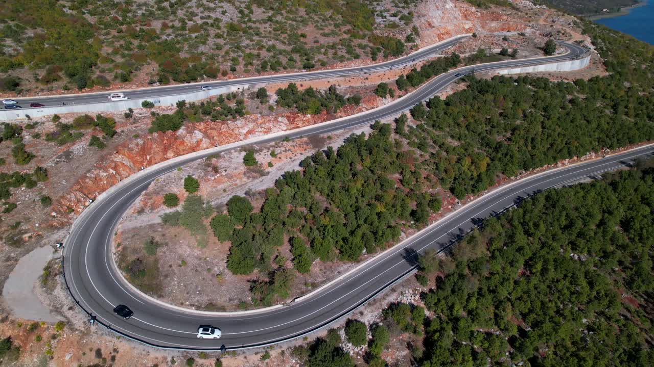 Auto che percorrono una strada panoramica tortuosa vicino a un bellissimo lago, ripresa aerea circolare.