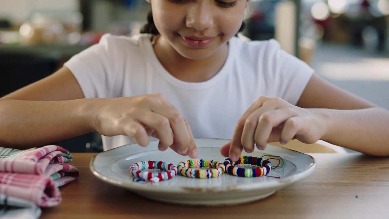 Noticing bracelets on plate, girl in white T-shirt handling and arranging them to inspect at cafe