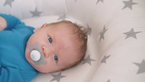 cute-kid-with-blue-eyes-sucks-pacifier-in-cocoon-at-home