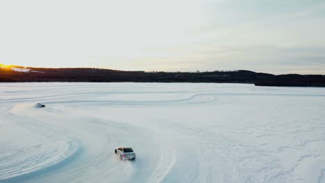 toma de drones de dos autos deportivos conduciendo en un lago congelado durante la puesta de sol en el círculo polar ártico.