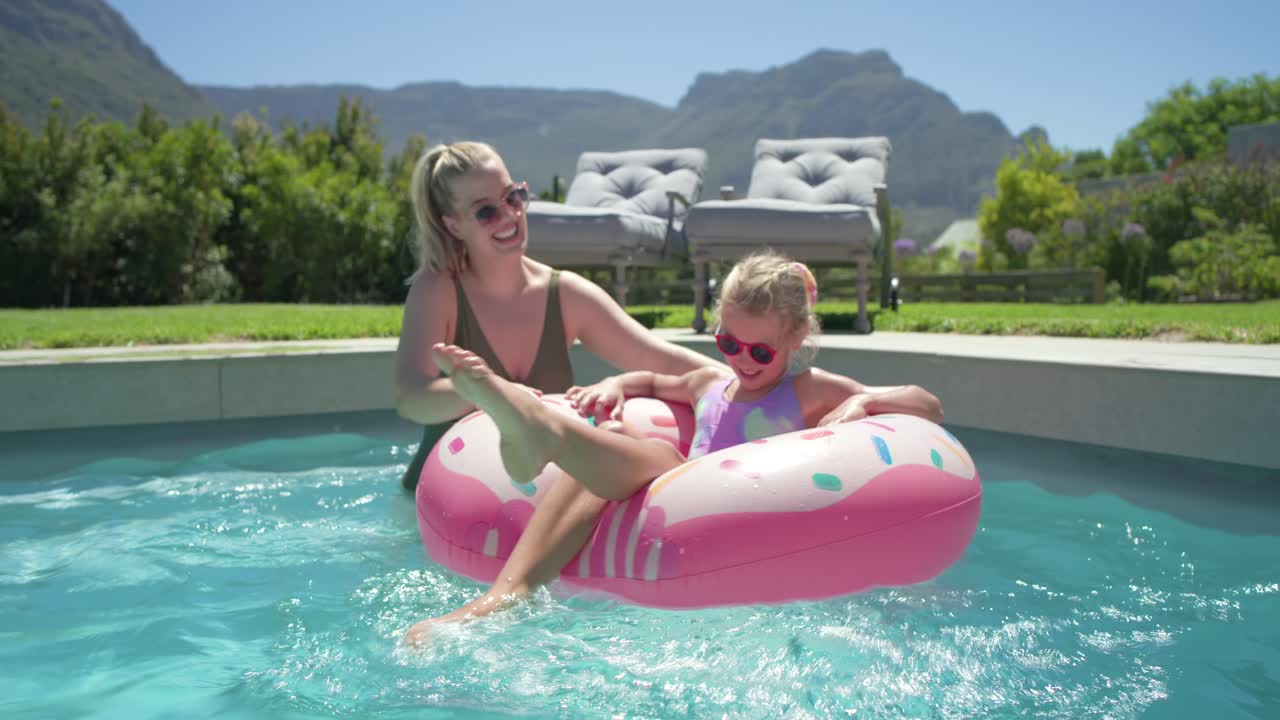 Mother guiding pink donut float after child settling at home pool, in swimsuit, encouraging kicking