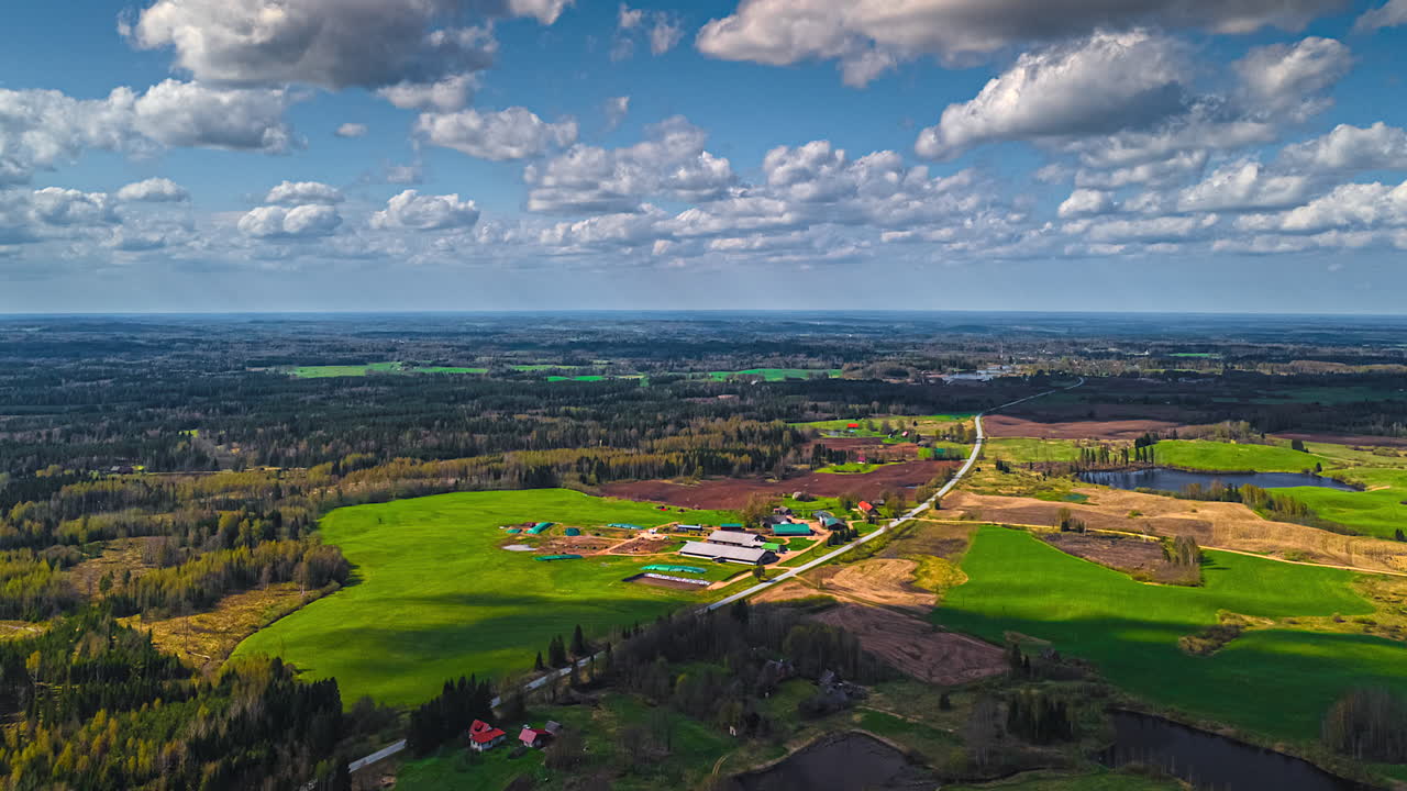 Farm village, meadows, fields, and forested landscape under clouds casting shadows as they blow by in this aerial time lapse