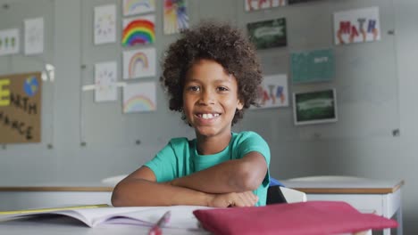 Video-of-happy-biracial-boy-sitting-at-desk-in-classsroom