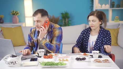 la pareja casada está desayunando en el desayuno, el hombre que está ocupado con su trabajo está hablando por teléfono y su esposa no está feliz con este evento.