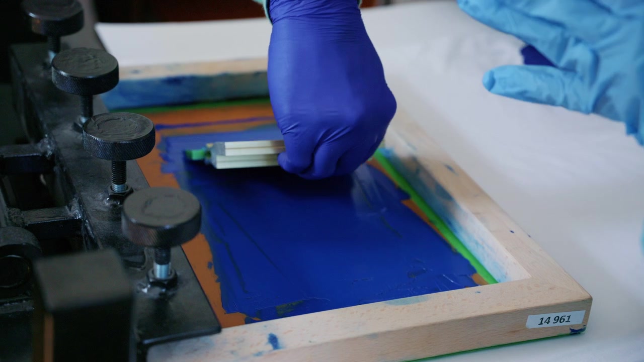 Worker using a squeegee to spread ink across a screen printing frame during textile production