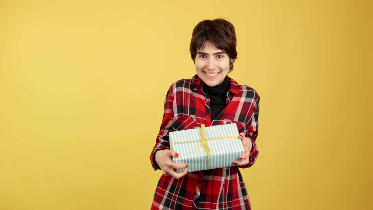 Woman with short hair smiling and holding a gift box against a yellow background
