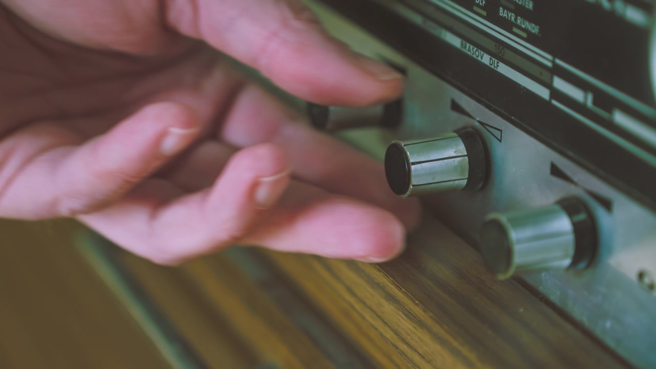 Nærbillede af hænder, der betjener flere kontrolknapper på en tysk radiogram-radioafspiller fra 1970'erne. Nyttigt til retro-teknologi, lydudstyr og udsendelsestemaer