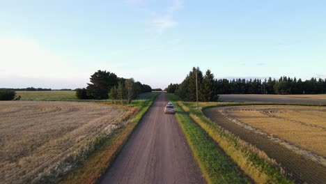 drone flying fast along a dry and dusty dirt road in rural alberta during sunset then passing a silver minivan parked on the side of the road