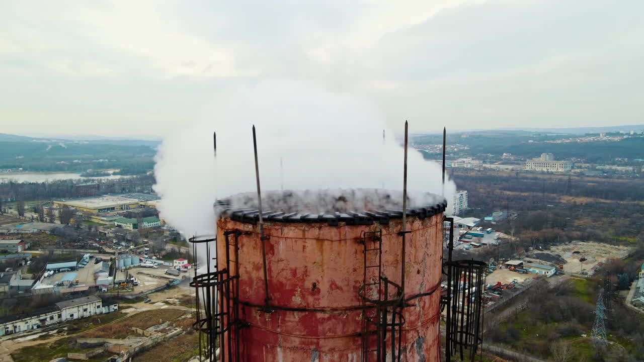 Aerial drone view of thermal station with smoke coming out of the tube. Buildings, roads and bare trees on the background. Cloudy weather. Chisinau, Moldova