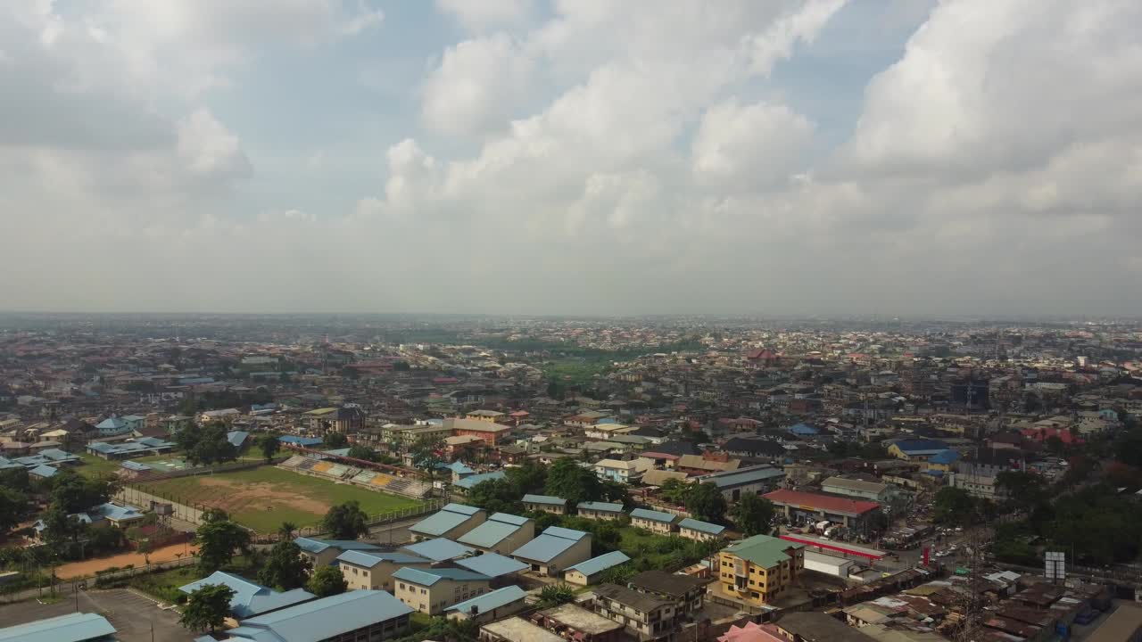 Vista aérea de uma comunidade em Lagos, Nigéria, em um dia nublado, com drone descendo para revelar uma rodovia com carros e caminhões em alta velocidade