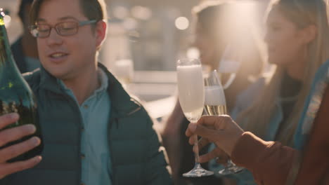 happy group of friends celebrating rooftop party drinking alcohol young man pouring champagne enjoying reunion celebration at sunset