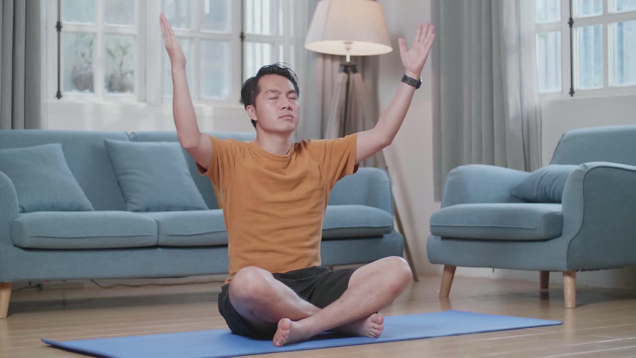 아시아인 남자가 집에서 마트 위에서 수카사나 요가 포즈를 취하고 있습니다.