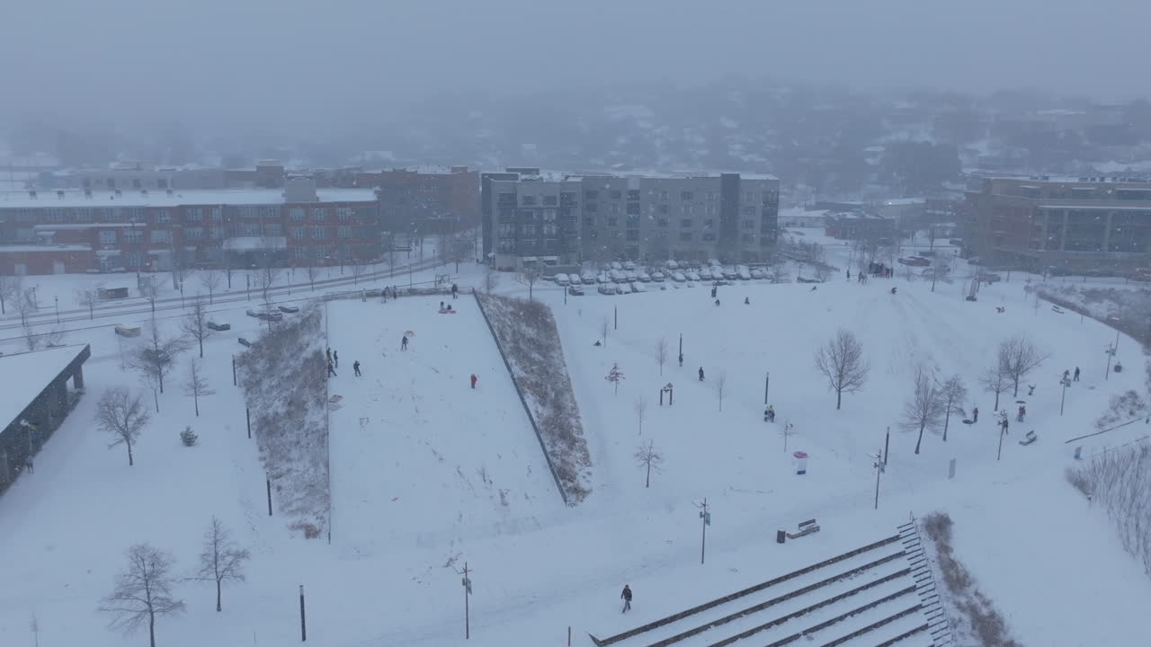 Aerial footage during a snowstorm in Chattanooga, TN of Renaissance Park with groups of people on a hill sledding.