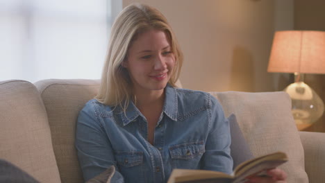 Mujer-Relajada-En-Casa-Por-La-Noche-Sentada-En-El-Sofá-Y-Leyendo-Un-Libro---Filmada-En-Cámara-Lenta