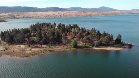 vista aérea hacia la isla del león en el lago jindabyne, día soleado, en australia - inclinación, disparo de drones