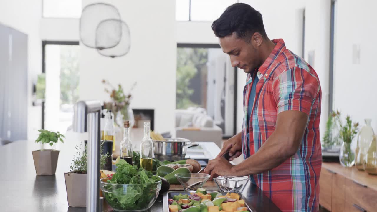 hombre biracial preparando comida, cortando verduras en una cocina moderna soleada, espacio de copia, cámara lenta