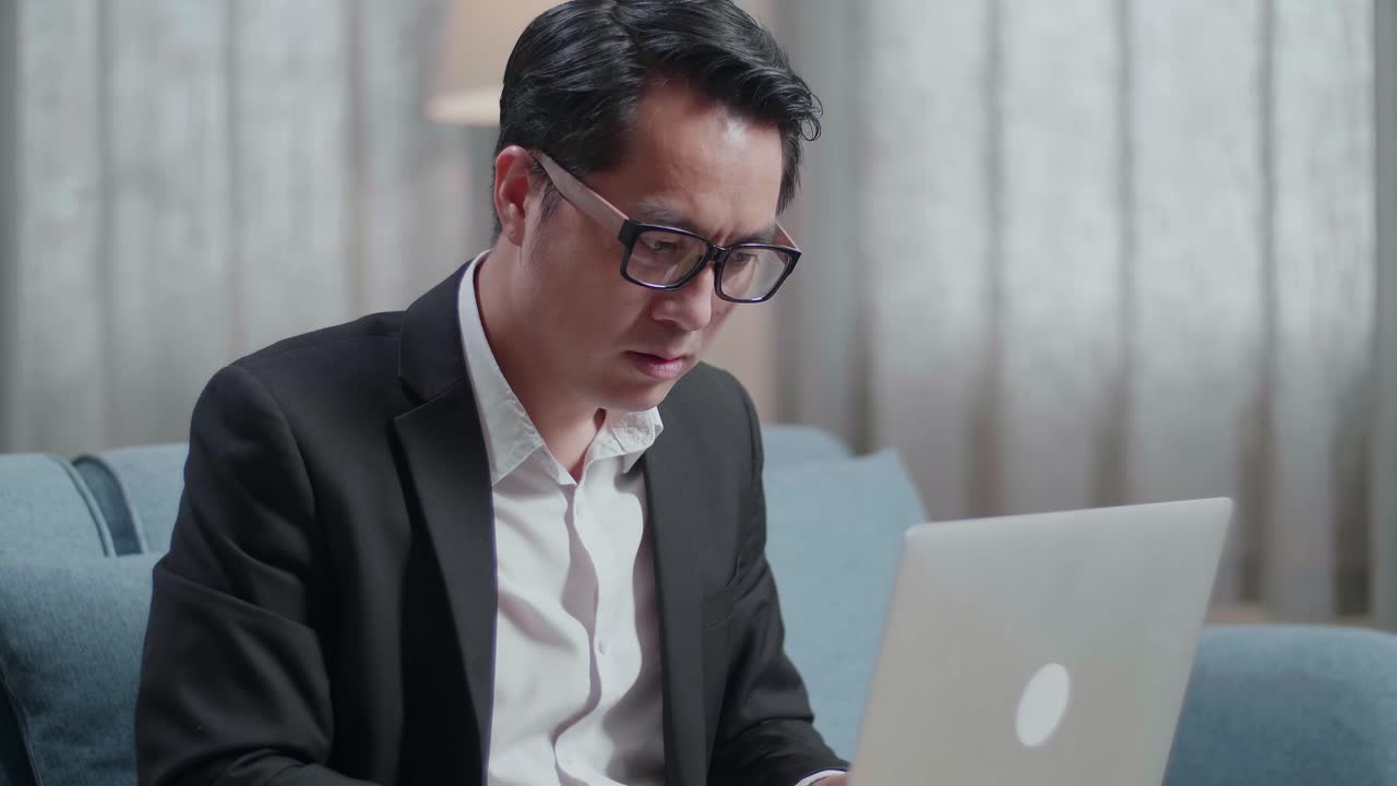 un hombre de negocios asiático en chaqueta y pantalones cortos está cansado mientras trabaja con una computadora portátil en casa