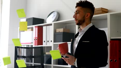 hombre de negocios en traje bebiendo de una taza cerca de la pared de vidrio