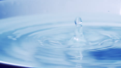 Echte-Wassertropfen-Fallen-In-Wasser-Und-Divergierende-Wasserkreise-Mit-Glattem-Farbhintergrund-Im-Studio-Mit-Kopierraum-Für-Die-Platzierung-Eines-Werbetextes