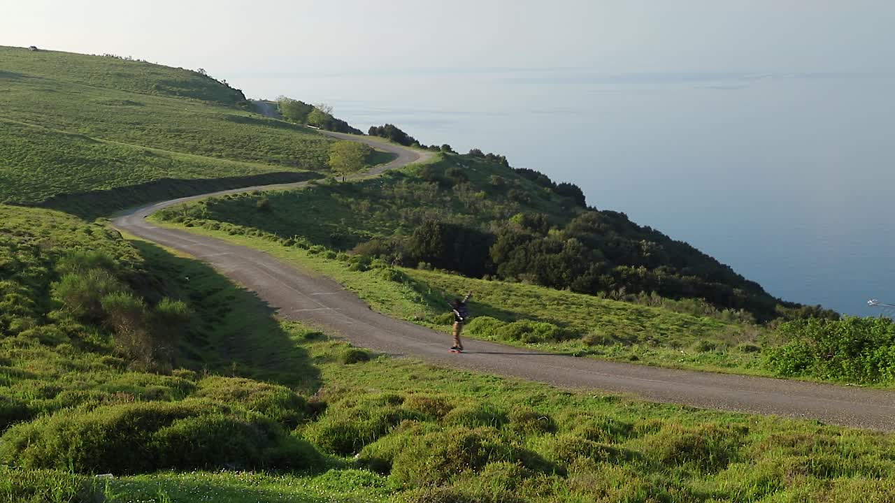 푸른 바다 옆에 있는 해변의 언덕을 통해 화려한 페니, 스케이트보드를 타고 내려가는 행복한 남자