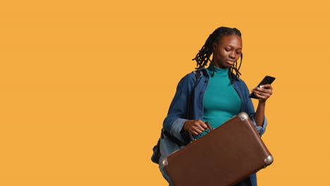 Smiling-girl-going-on-vacation-with-suitcase,-reading-texts,-studio-background