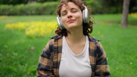 Close-up-of-a-happy-girl-with-curly-hair-in-white-wireless-headphones-resting-and-listening-to-music-in-the-park