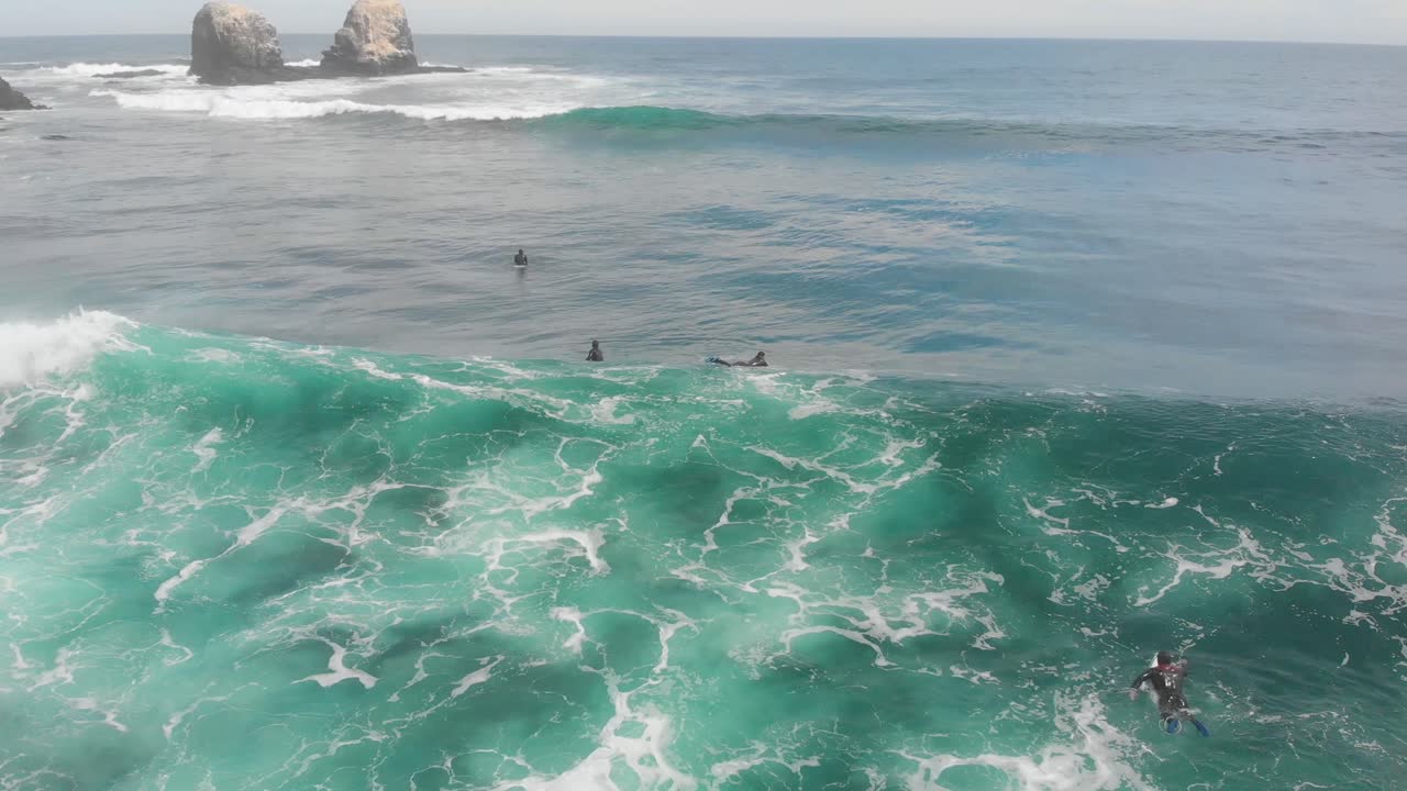 Aerial flying backwards of turquoise wave with rocky formations on the background on a sunny dat, Pichilemu, Chile-4K