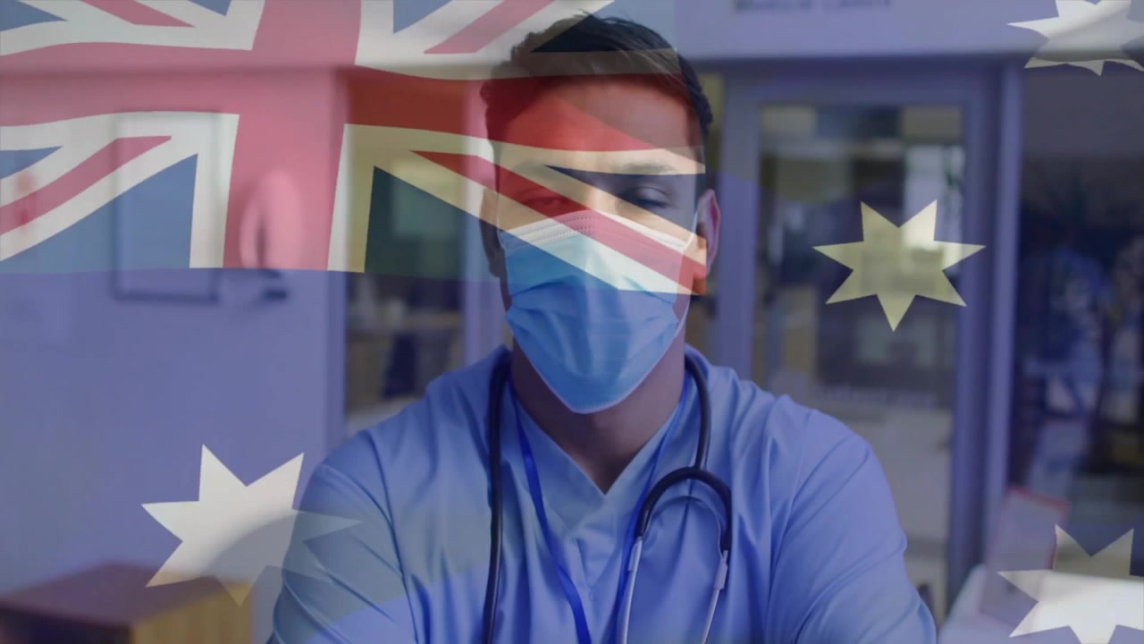 Eine australische Flagge verblasst, während ein männlicher Kliniker an der Rezeption den Kopf neigt und den Blick wechselt, um Fürsorge zu zeigen.