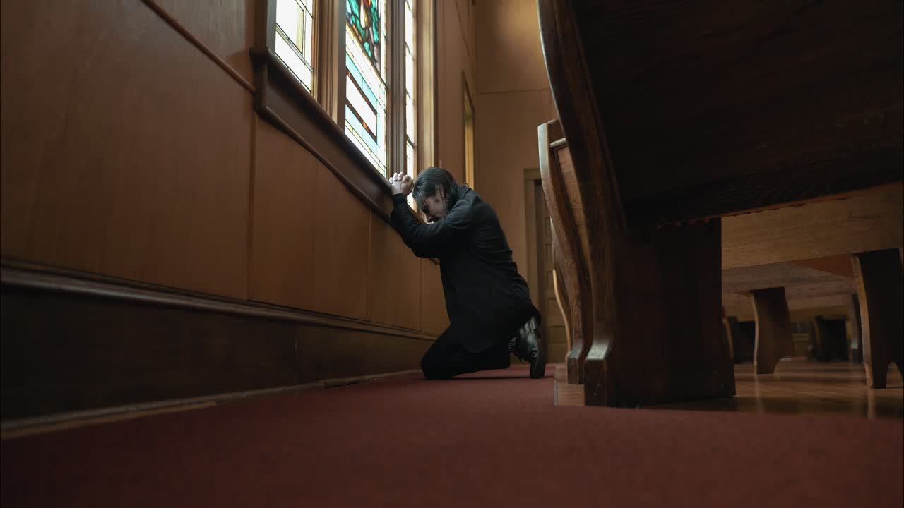 A Christian man, priest, preacher, pastor praying on his knees inside old church building, creating a cinematic and contemplative mood