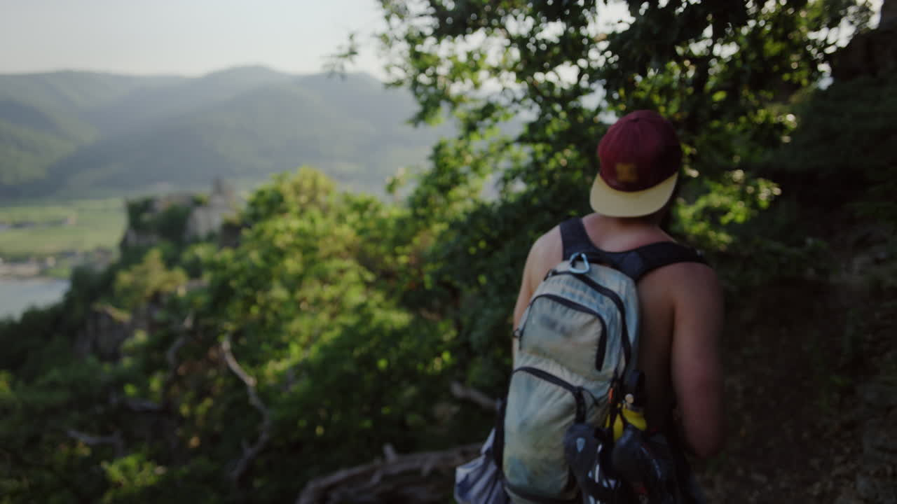 hombre joven guapo camina paisaje de montaña, cámara lenta, hombre con mochila, pecho desnudo, sendero de senderismo, ruta de montaña, valle del bosque verde, tiempo soleado, austria, durnstein, europa, slomo cinematográfico