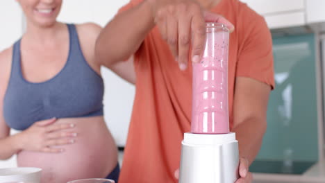 preparing smoothie, pregnant woman and partner in kitchen together smiling