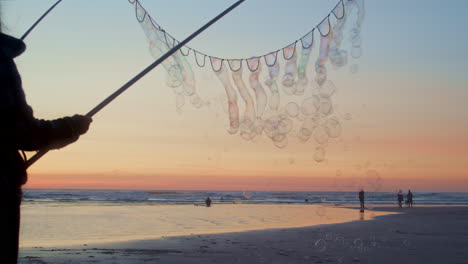 bubbles float across sunset beach sky from person with bubble wand