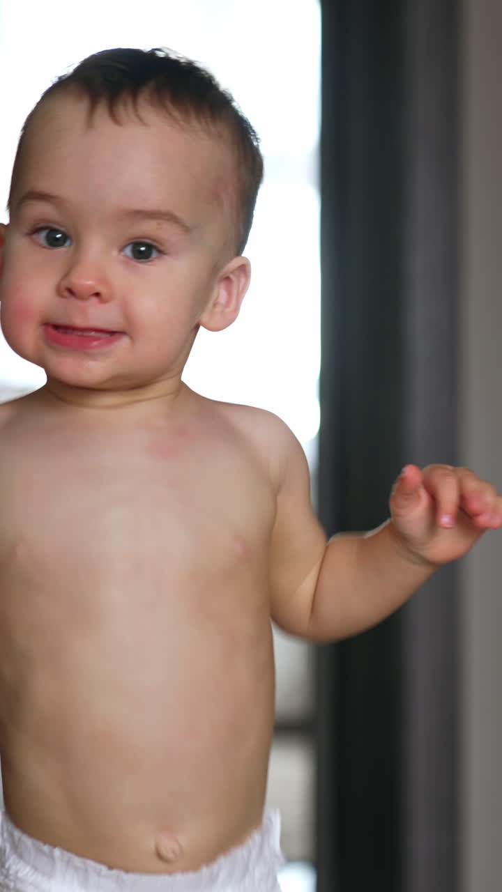 Smiling Caucasian baby in diaper running up to camera. Lovely kid being active at home. Vertical video