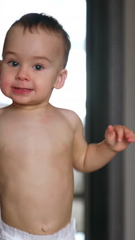 smiling caucasian baby in diaper running up to camera. lovely kid being active at home. vertical video