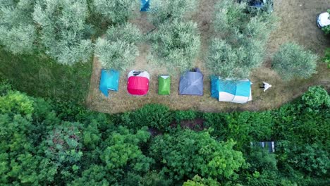 top down ascending view of a camping site in a green field in italy, with a man walking out