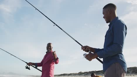 african american senior father and two teenage sons standing on a beach fishing and talking