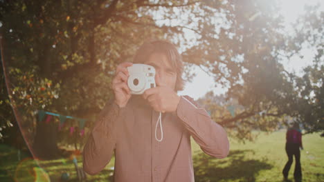 man taking a photo with instant camera in a park