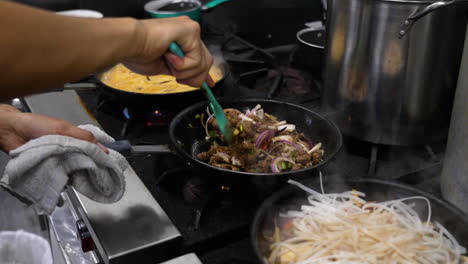 cinematic shot following a line of simmering skillets filled with various menu items, cook tosses and stirs beef and onions in sizzling skillet, slow motion slider 4k