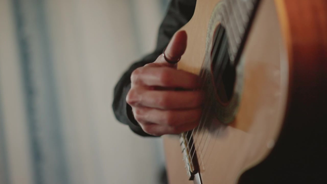 Closeup acoustic pick near soundhole, delicate strum practice by guitarist in cozy home studio, soft natural light, nylon strings, instruction vibe, close finger movements, focus on right hand