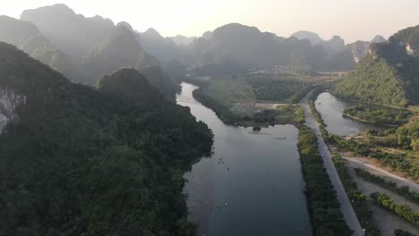 vista aérea de un avión no tripulado en vietnam volando sobre un valle rodeado de montañas rocosas cubiertas de árboles verdes sobre un río en ninh binh en un día soleado