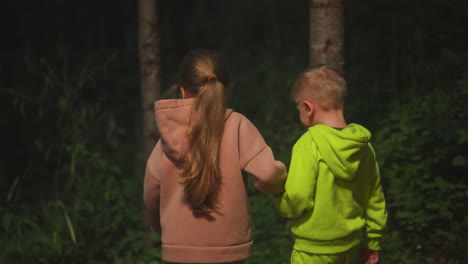 little children walk through night forest together. curious brother and sister join hands walking across wild park in evening. happy kids on vacation