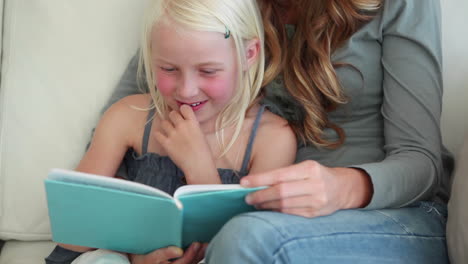 girl laughing as she is reading a book with her mother