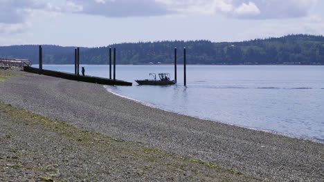 Small,-nondescript-fishing-boat-cruising-past-beach-at-Camano-Island-State-Park,-WA-State