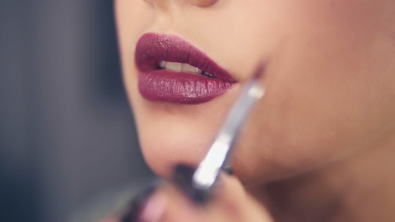Close Up view of a professional makeup artist's hand using special brush to apply lipstick or lipgloss on model's lips working