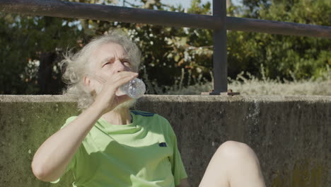 homme senior fatigué assis sur un terrain de football et de l'eau potable