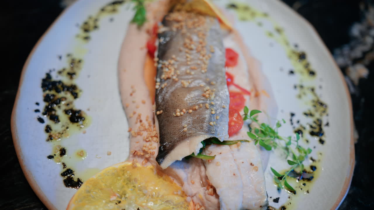 Close up of a beautifully plated fish fillet with sauce, lemon slice, and herbs