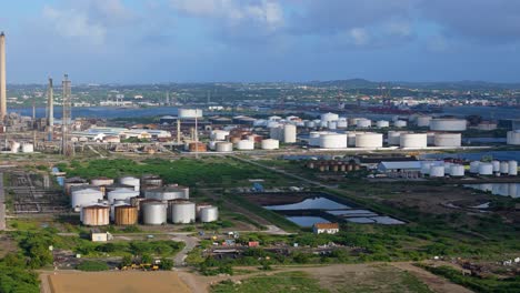 large storage tanks of oil refinery line up in rows below flare stacks in curacao